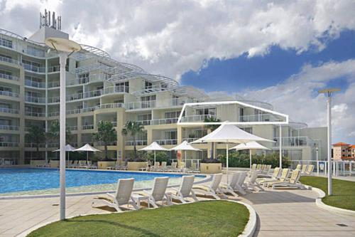 a pool with chairs and umbrellas in front of a large building at Ettalong Beach Luxury Apartments in Ettalong Beach