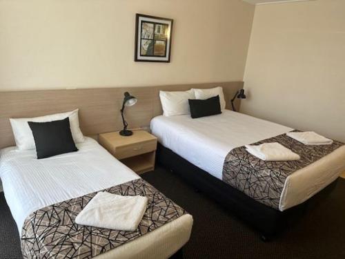 a hotel room with two beds and a lamp at City Centre Motel Kempsey in Kempsey