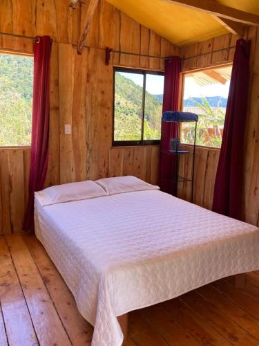 a bed in a wooden room with two windows at Mario´s Lodge Providencia in El Copey