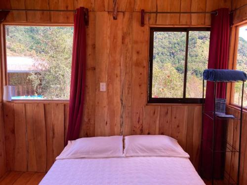 a bed in a wooden room with two windows at Mario´s Lodge Providencia in El Copey