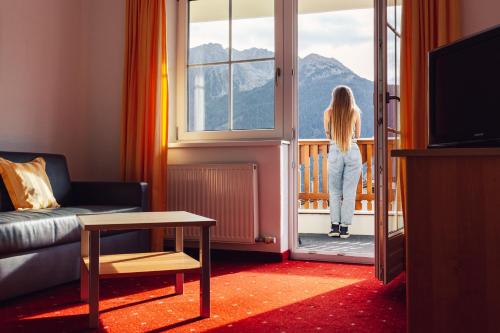 a woman standing on a balcony looking out the window at Hotel Alpen-Royal in Jerzens