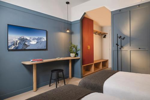 ein Schlafzimmer mit einem Bett und einem Schreibtisch mit einem Monitor an der Wand in der Unterkunft Hôtel de la Couronne in Chamonix-Mont-Blanc