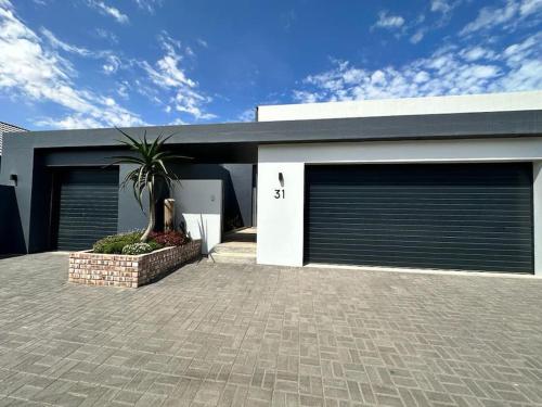 a house with two garage doors and a palm tree in front at The Elegant Beach House in Swakopmund