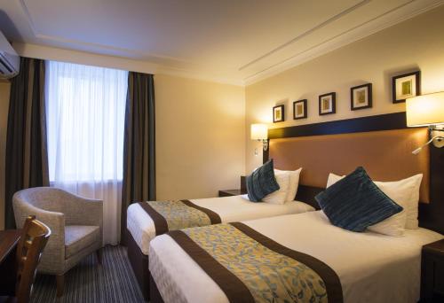 um quarto de hotel com duas camas e uma cadeira em Thistle London Heathrow Terminal 5 em Hillingdon