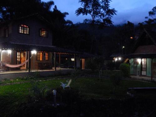 una casa iluminada por la noche con un banco en el patio en Recanto beira rio - Sao Pedro da serra. en Nova Friburgo