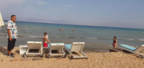 a man standing on a beach with chairs and people in the water at Panorama Lodge Nuweiba in Nuweiba