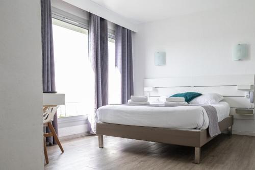 a white bedroom with a bed and a window at Hotel Aquarius in Canet-en-Roussillon