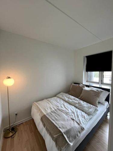 a white bedroom with a bed with a lamp and a window at Moderne lejlighed i hjertet af Odense C in Odense