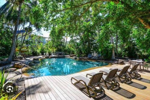 a swimming pool with lounge chairs and trees at Hamilton Island Poinciana 008 Ground Floor 2bedrooms Free Buggy in Hamilton Island
