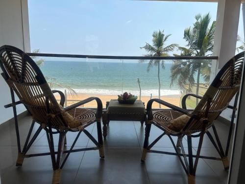 two chairs and a table with a view of the beach at Sunset and Palm trees - An Airport Boutique by the Sea in Trivandrum