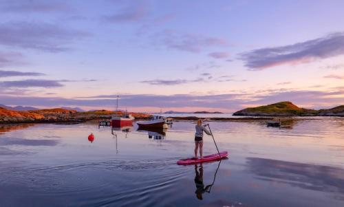 a woman standing on a paddle board in the water at Rorbu i Bud Havn in Bud