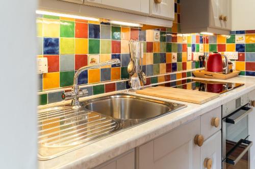 una cocina con fregadero de acero inoxidable y azulejos coloridos en Carters cottage, en Buckinghamshire