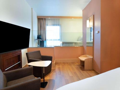 Habitación de hotel con cama, TV y sillas en Ibis Madrid Centro las Ventas en Madrid
