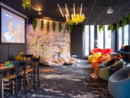 a room with people sitting on chairs and a large screen at ibis Styles Strasbourg Nord Palais des Congrès in Schiltigheim