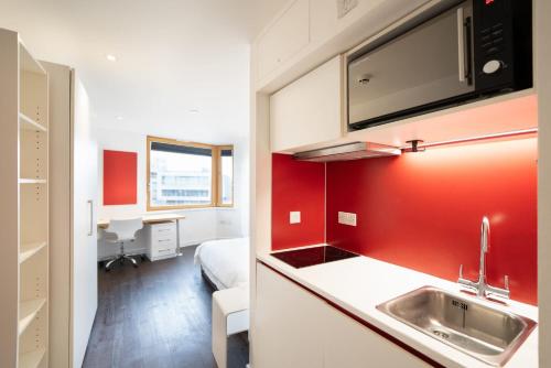 a kitchen with a sink and a red wall at Cosy Studios and Apartments at Chapter Aldgate in London in London