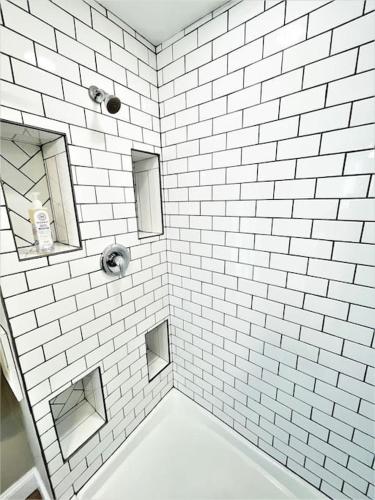 a white tiled bathroom with a tub and a mirror at The loft at Park Place - 3rd floor walk up King and Queen beds fast WIFI and free coffee in Wilmington
