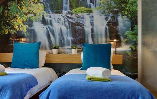 dwa łóżka z niebieskimi poduszkami przed malowidłem wodospadowym w obiekcie Condomínio Zen Pearl-Luxury com piscina w Funchal