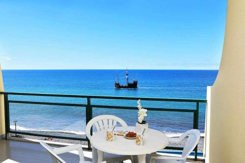 a table and chairs with a boat in the ocean at Formosa Sunset - Em frente à praia com wifi in Panasqueira