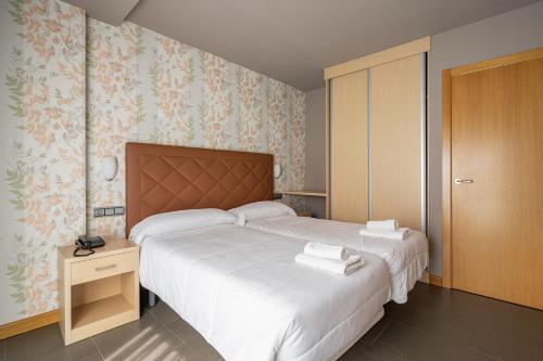 1 dormitorio con 2 camas con sábanas blancas y papel pintado con motivos florales en Apts Spa Cueto 3d 4 adultos, en Cangas de Onís