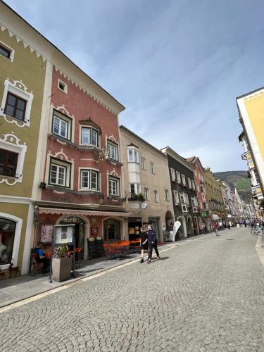 two people walking down a city street with buildings at goldenes kreuz in Vipiteno