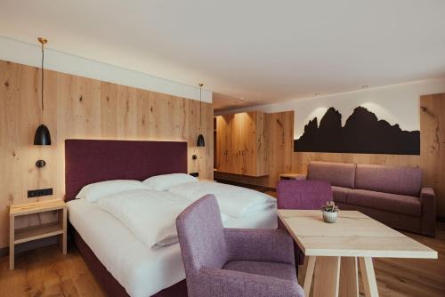 a bedroom with a large white bed and purple chairs at Hotel Digon in Ortisei