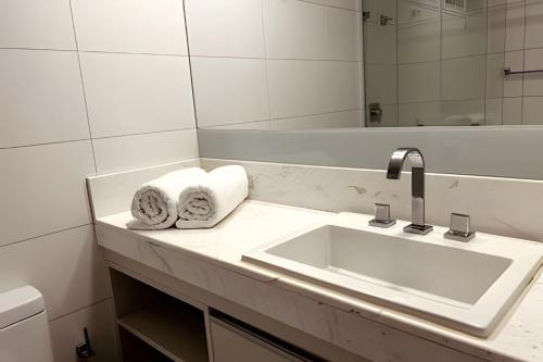 La salle de bains blanche est pourvue d'un lavabo et d'un miroir. dans l'établissement Apto 2Q com vista para o mar no Solar Tambaú, à João Pessoa
