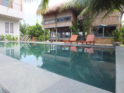 a swimming pool with two chairs and a house at Home Farm Villa Hoi An in Hoi An