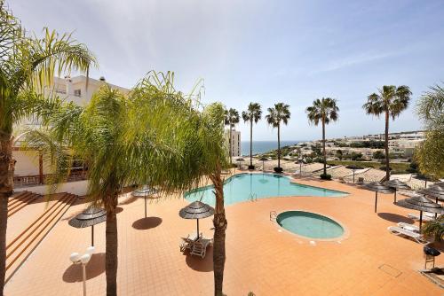 a swimming pool with umbrellas and palm trees and the ocean at Villa Mós - Beach Apartments in Lagos