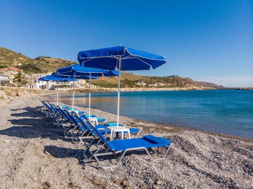 a group of blue chairs and umbrellas on a beach at Kyma beach - Apollon apartment - 2ad & 2kids in Kolymvari