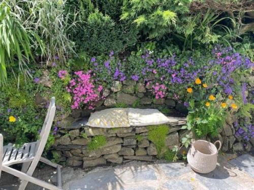 a stone wall with a bench and flowers at Bell Cottage in Saint Teath