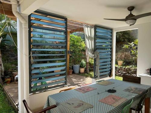 een kamer met een tafel en een raam met blauwe luiken bij Appt Althea avec Jardin privé proche lagon - La Saline-les-bains in Saint-Paul