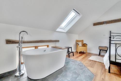uma banheira branca num quarto com uma clarabóia em Tumbledown Barn em Knowstone