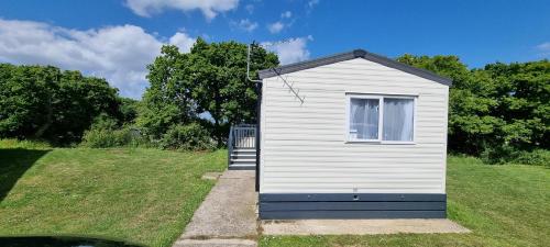 a small white shed sitting in a grass field at Beautiful Caravan With Decking Wifi At Isle Of Wight, Sleeps 4 Ref 84047sv in Porchfield