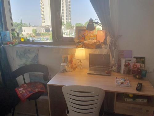 einen Schreibtisch mit einem Laptop und einem Stuhl neben einem Fenster in der Unterkunft נווה מדבר in Jerusalem