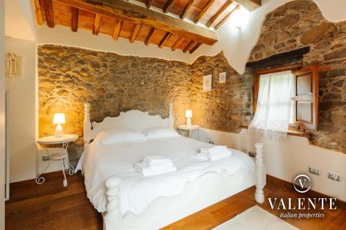 um quarto com uma cama branca e uma parede de pedra em Casa con vista panoramica, Matraia, Lucca em Matraia