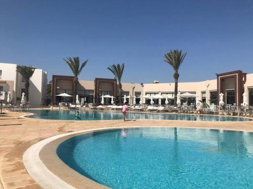 een groot zwembad in een resort met palmbomen bij Logement S+2 dans un hôtel 4* vue mer in Bizerte