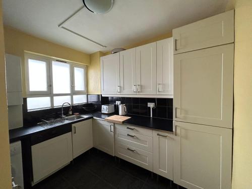 a kitchen with white cabinets and a black counter top at Super-convenient, 3 mins to Kings Cross in London