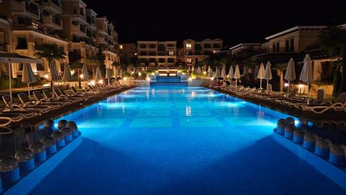 a large swimming pool with chairs and umbrellas at night at Sea and Sand Apartment Greenn Life in Sozopol