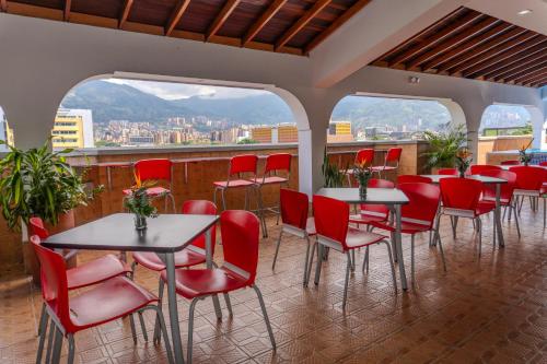 a restaurant with red chairs and tables and windows at Hotel Alcaravan Medellín in Medellín
