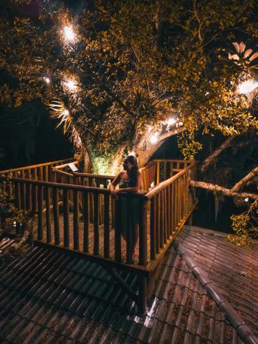 a woman standing on a wooden bridge under a tree at Pousada Equilíbrio dos Canyons in Praia Grande