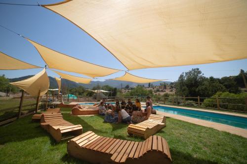 a group of people sitting under a large umbrella by a pool at Glamping, escapada en la naturaleza in San Clemente