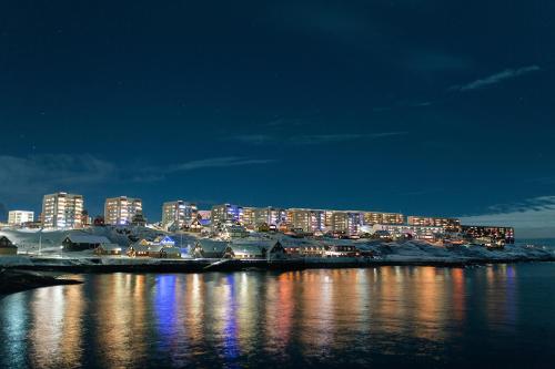 Una ciudad iluminada por la noche con el agua en Hotel Aurora Apartments, en Nuuk