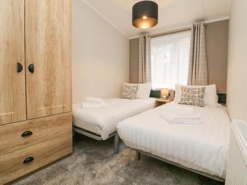 a bedroom with two beds and a cabinet and a window at 18 Manleigh Park in Ilfracombe