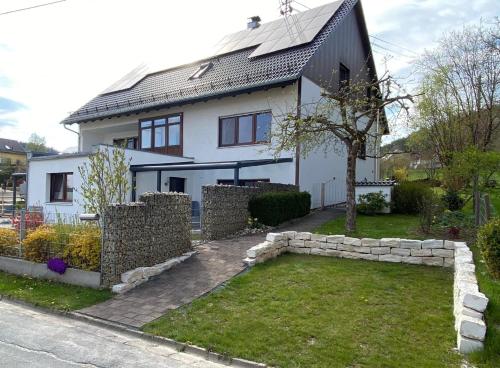 uma casa branca com uma parede de pedra em frente em Helle Ferienwohnung in Oberfellendorf mit Terrasse, Grill und Garten em Oberfellendorf