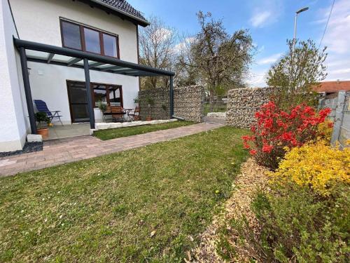 uma casa branca com um quintal com flores vermelhas em Helle Ferienwohnung in Oberfellendorf mit Terrasse, Grill und Garten em Oberfellendorf
