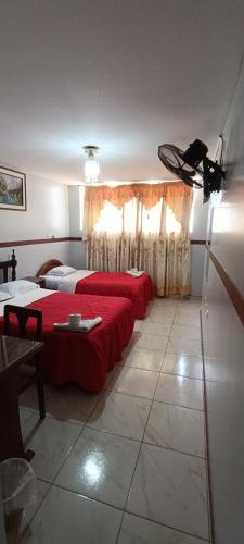 a bedroom with two beds with red sheets and a table at HOTEL LAS GARDENIAS in Trujillo