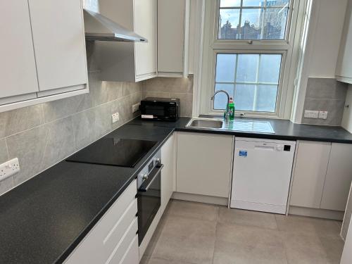 cocina con armarios blancos, fregadero y ventana en Kings Cross Guest House, en Londres