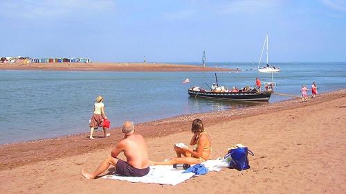 Stokeinteignhead的住宿－Ferienhaus für 2 Personen ca 50 qm in Stokeinteignhead, England Südküste von England，坐在海滩上的男人和女人,坐船