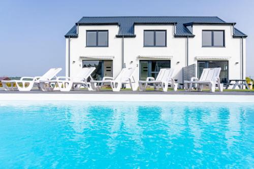 a house with white chairs and a swimming pool at Cichy Domek - Podgrzewany Basen, Parking, Aneks Kuchenny in Karwia