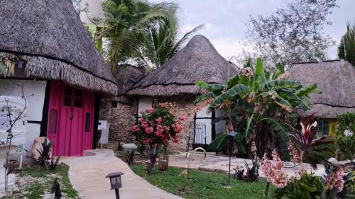 a group of houses with thatched roofs and a pink door at Hotel y Museo Aldea Maya Toktli Orígenes - Casa Maya Melipona - Alberca, Wifi Starlink, Tour Museo in Izamal